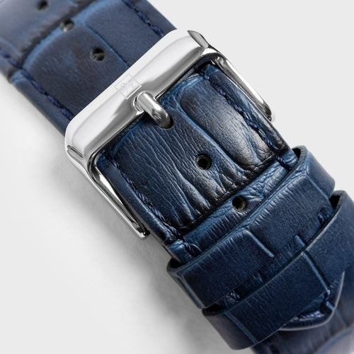 Close-up of a blue leather watch strap with a silver buckle on a light gray background