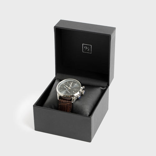 Watch in a black box with a visible brand logo on a light gray background