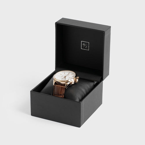 Watch in a black box with a visible brand logo on a light gray background