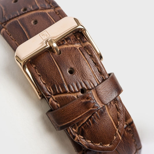 Brown leather watch strap with gold buckle on a light gray background