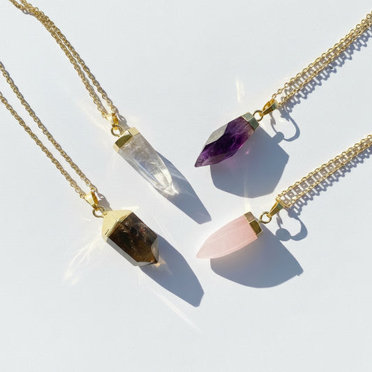 Three gold necklaces with crystal pendants on a white background